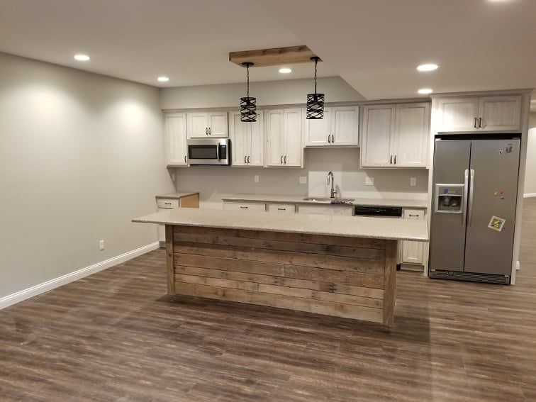A modern kitchen with white cabinets, a stainless steel refrigerator, and a kitchen island with a rustic wood base.