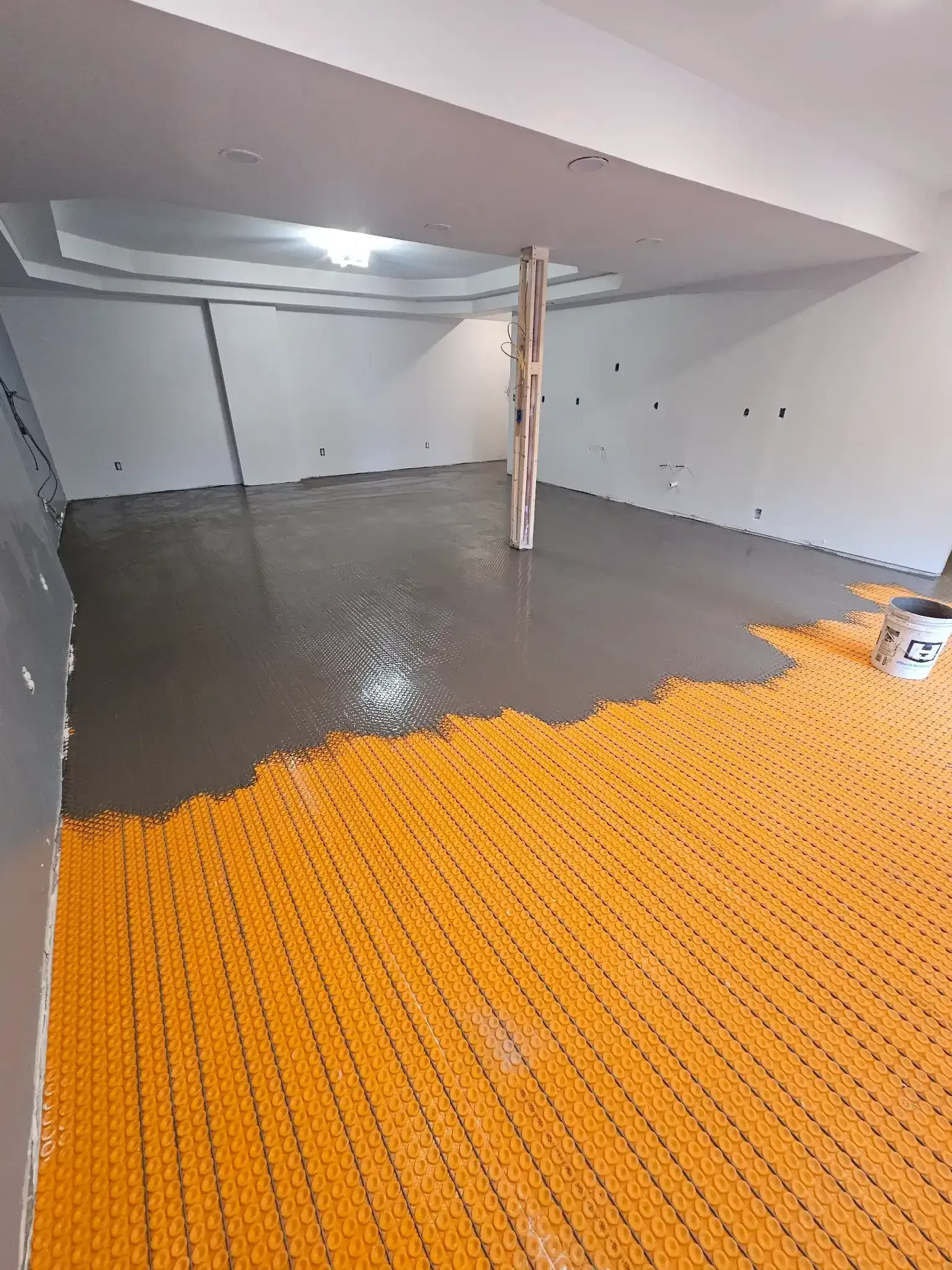 A room under renovation with a half-covered floor showing orange heating mats and a freshly poured layer of gray screed.