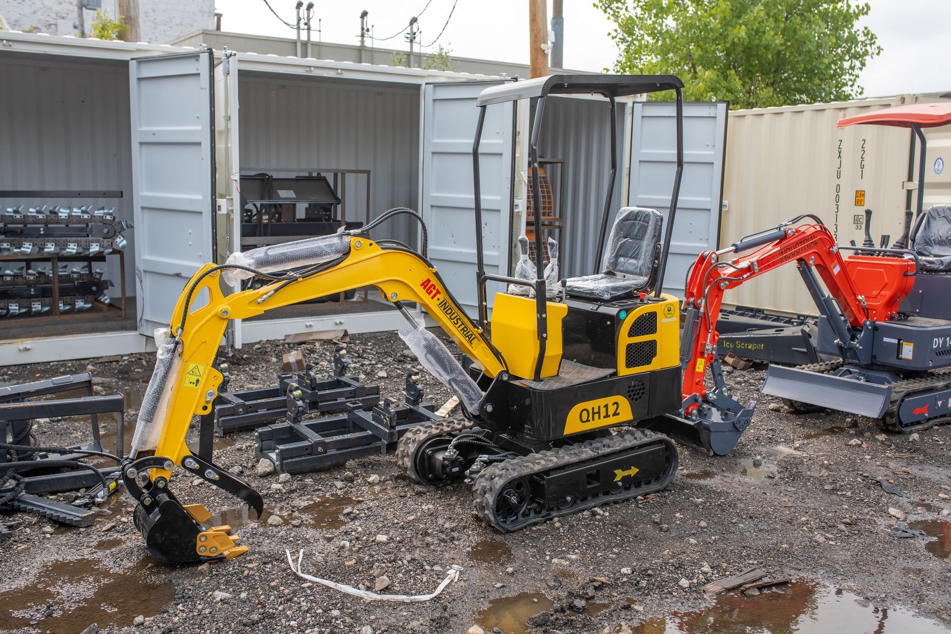 Yellow and black mini excavator with exposed tracks, parked outdoors. Next to a smaller red excavator.