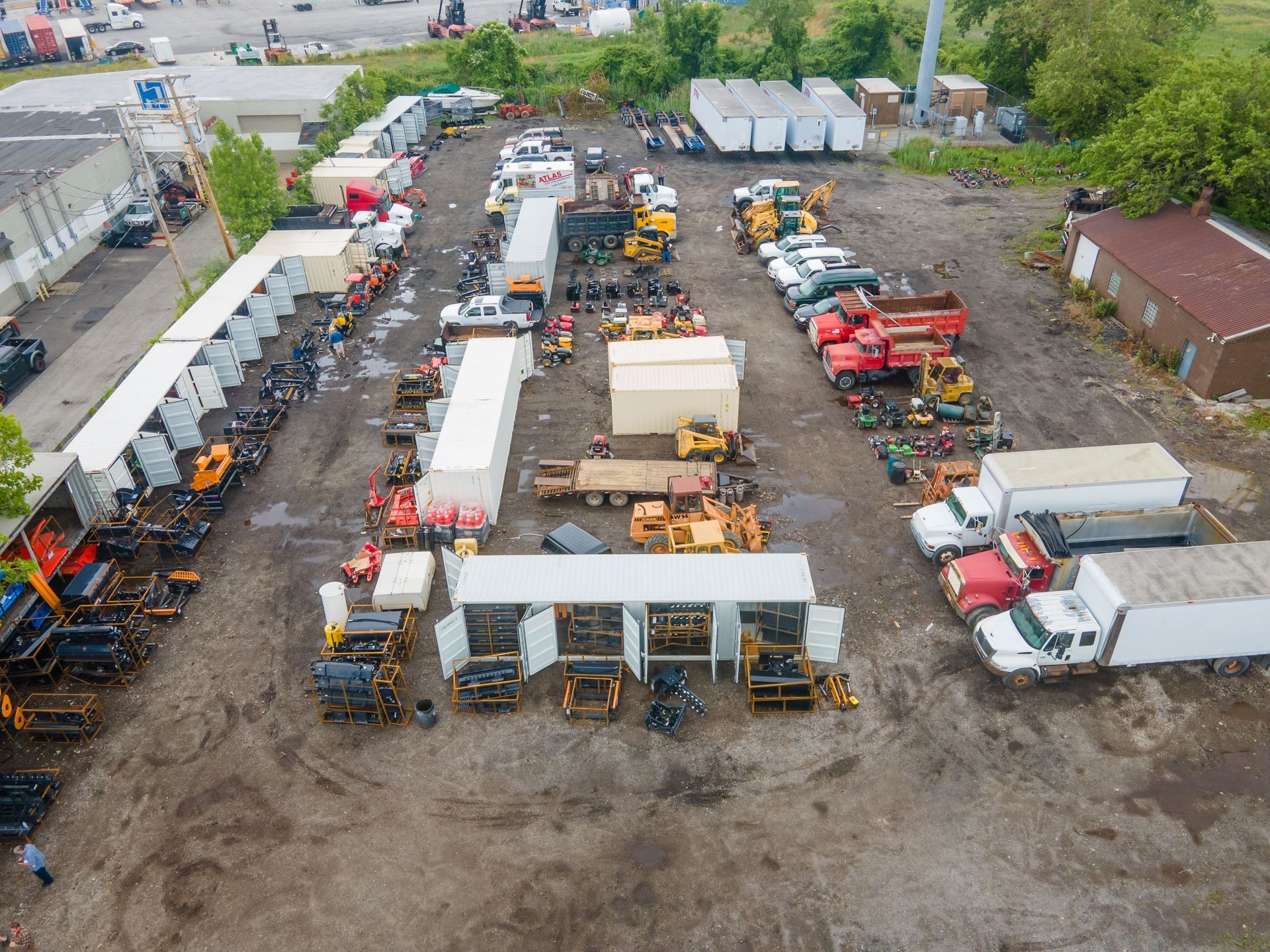 Aerial view of a lot filled with heavy machinery and trucks; white canopies provide some shade.