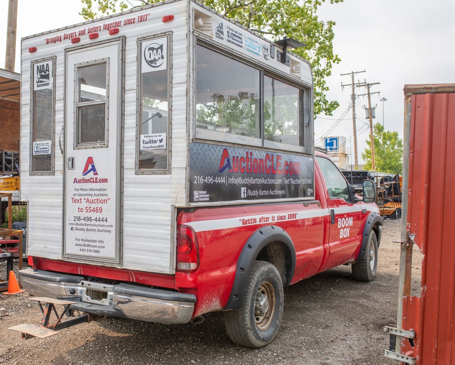 Red truck with white camper shell, parked outdoors. The shell has windows and business signage.