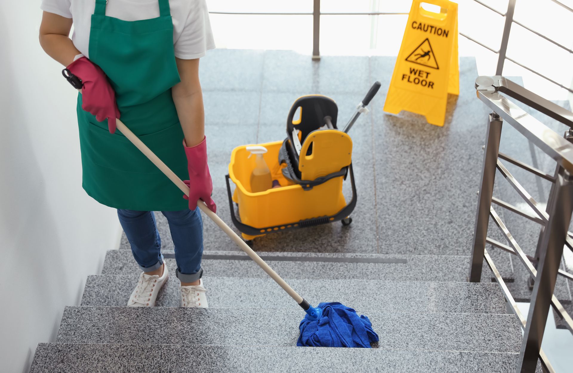 Person mopping stairs near a wet floor sign and cleaning supplies.