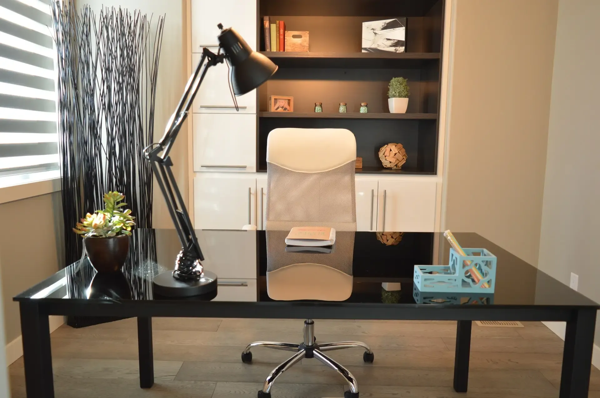 Modern home office with black desk, lamp, chair, and built-in shelving.