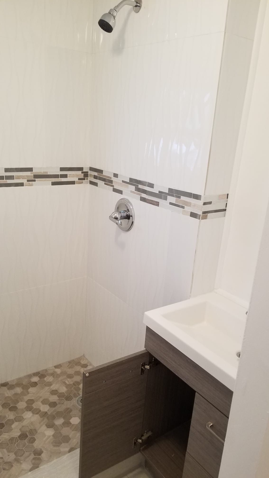 Bathroom with white tiled shower, decorative border, and vanity. Open cabinet door.