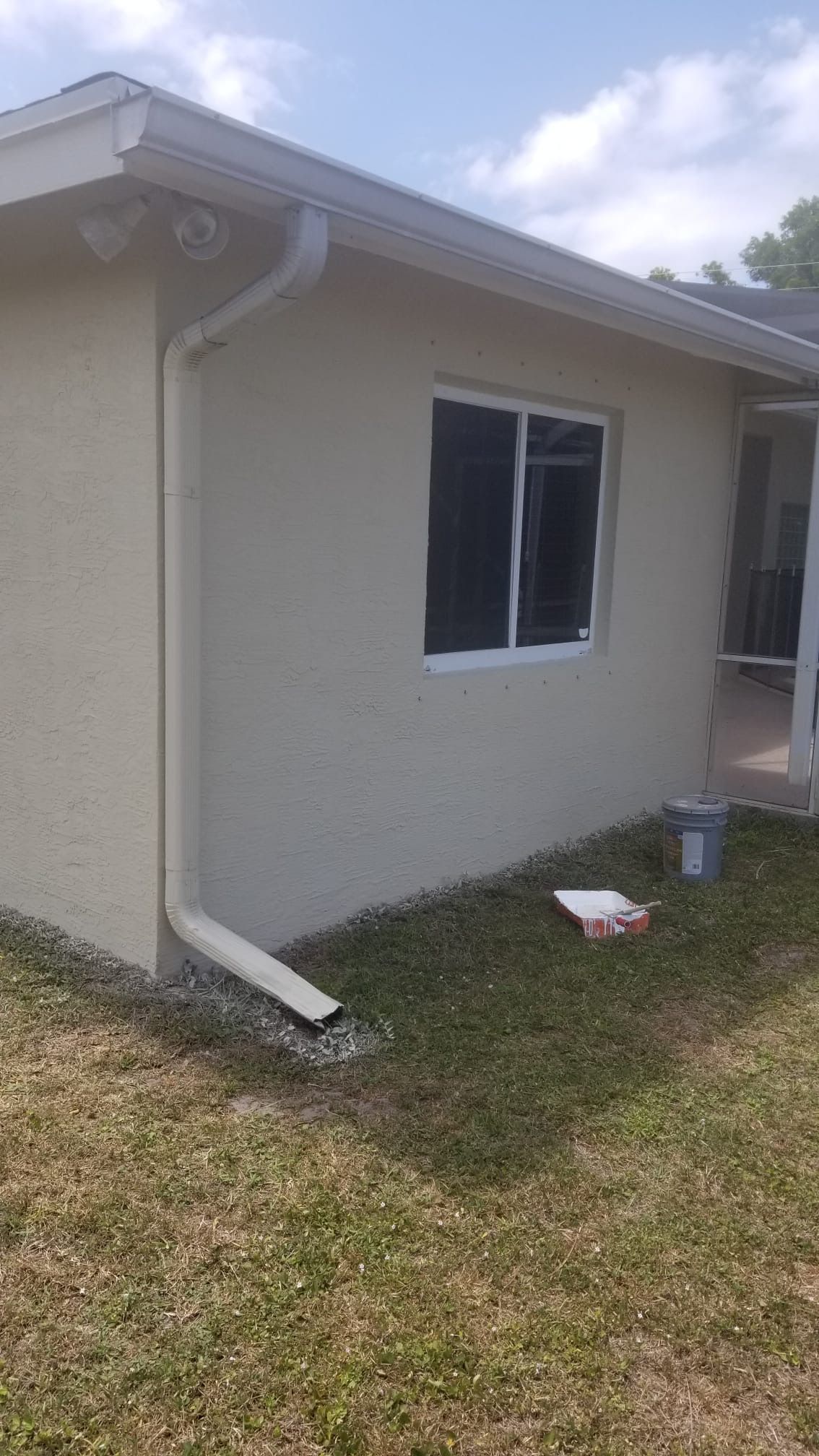 Beige stucco house with white trim, gutters, window, and downspout.
