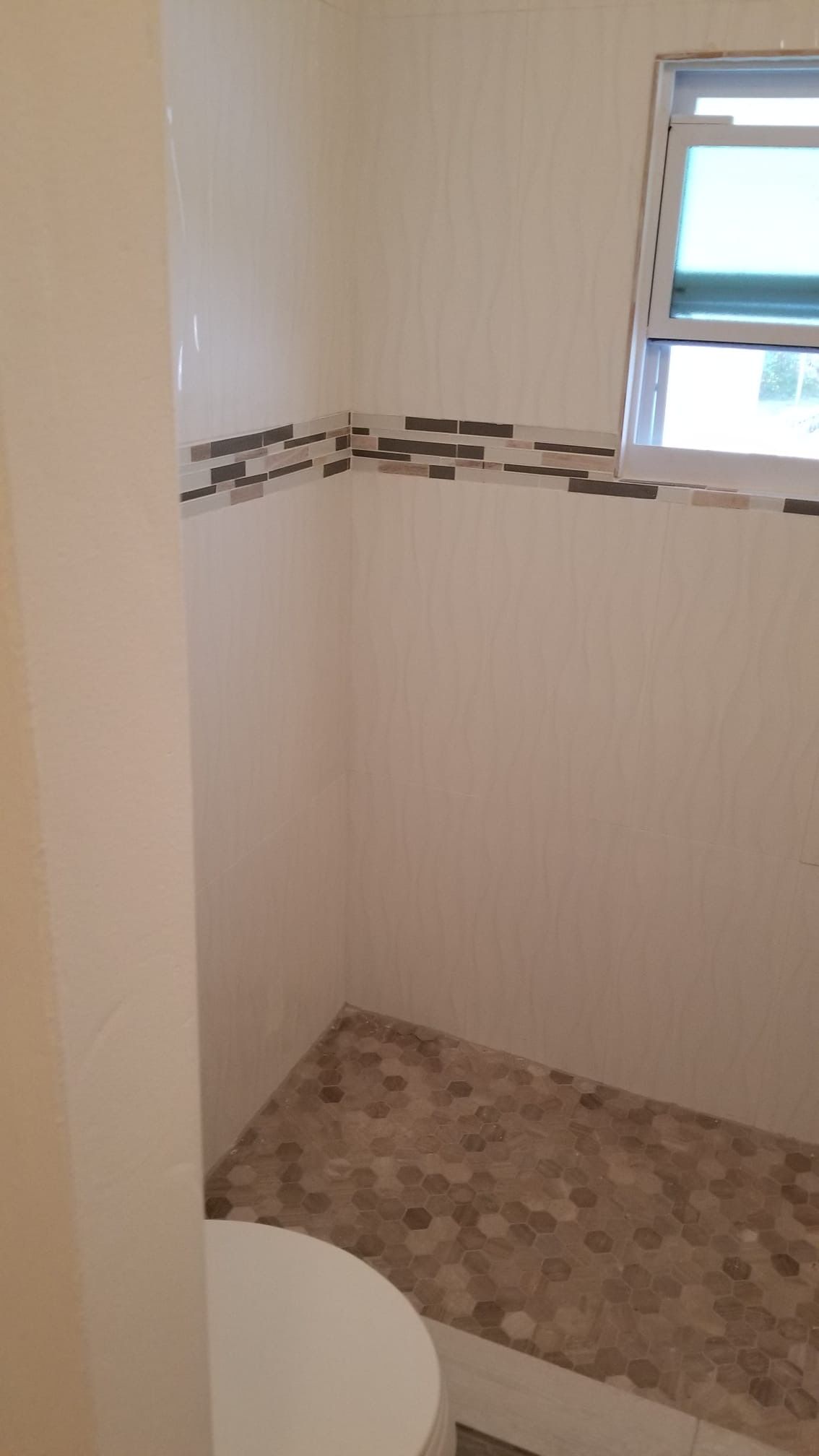 Shower stall with pebble floor, beige walls, mosaic tile border, small window.