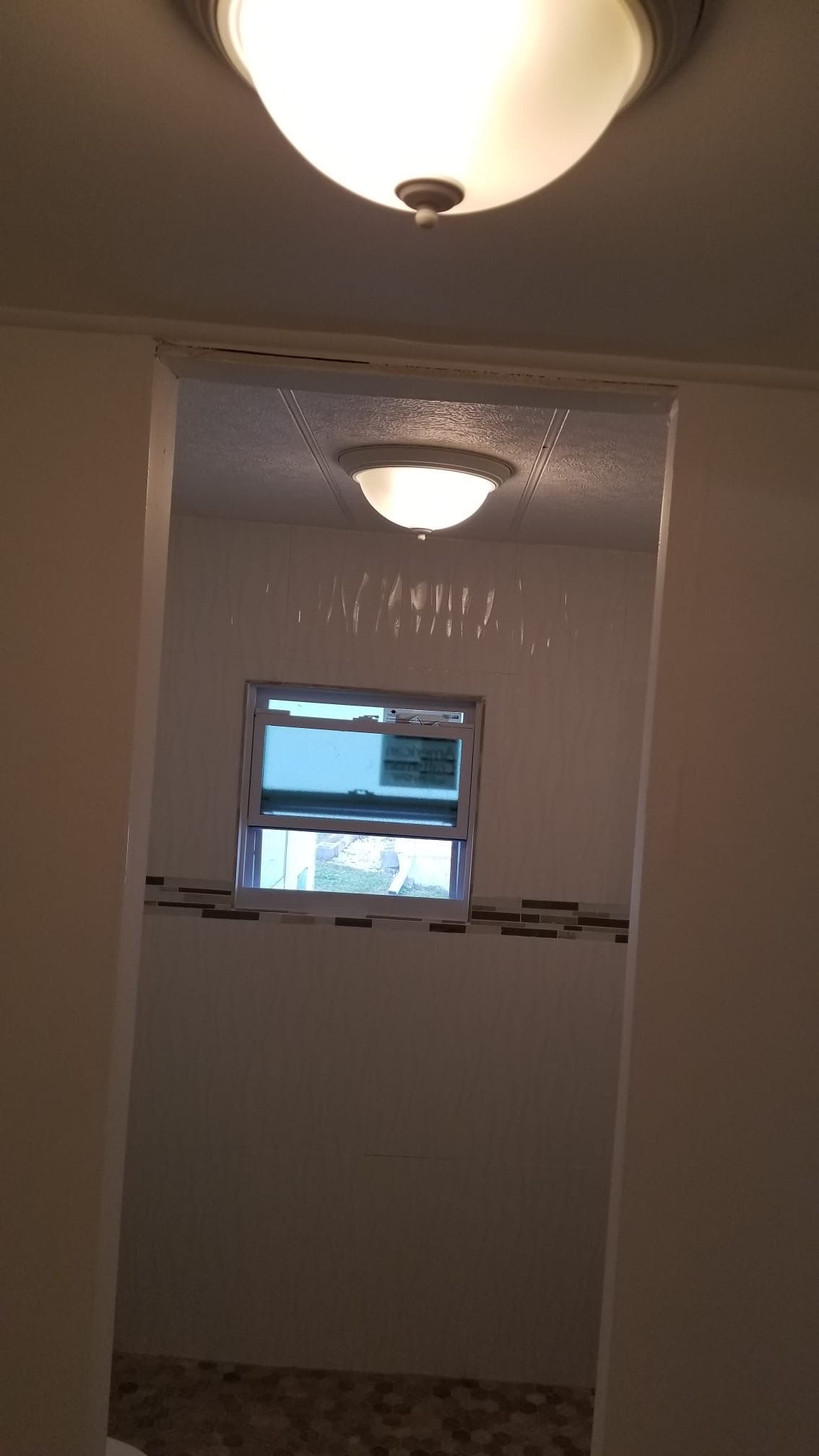A doorway leads to a bathroom with a window and a light fixture; white walls and a tile border.