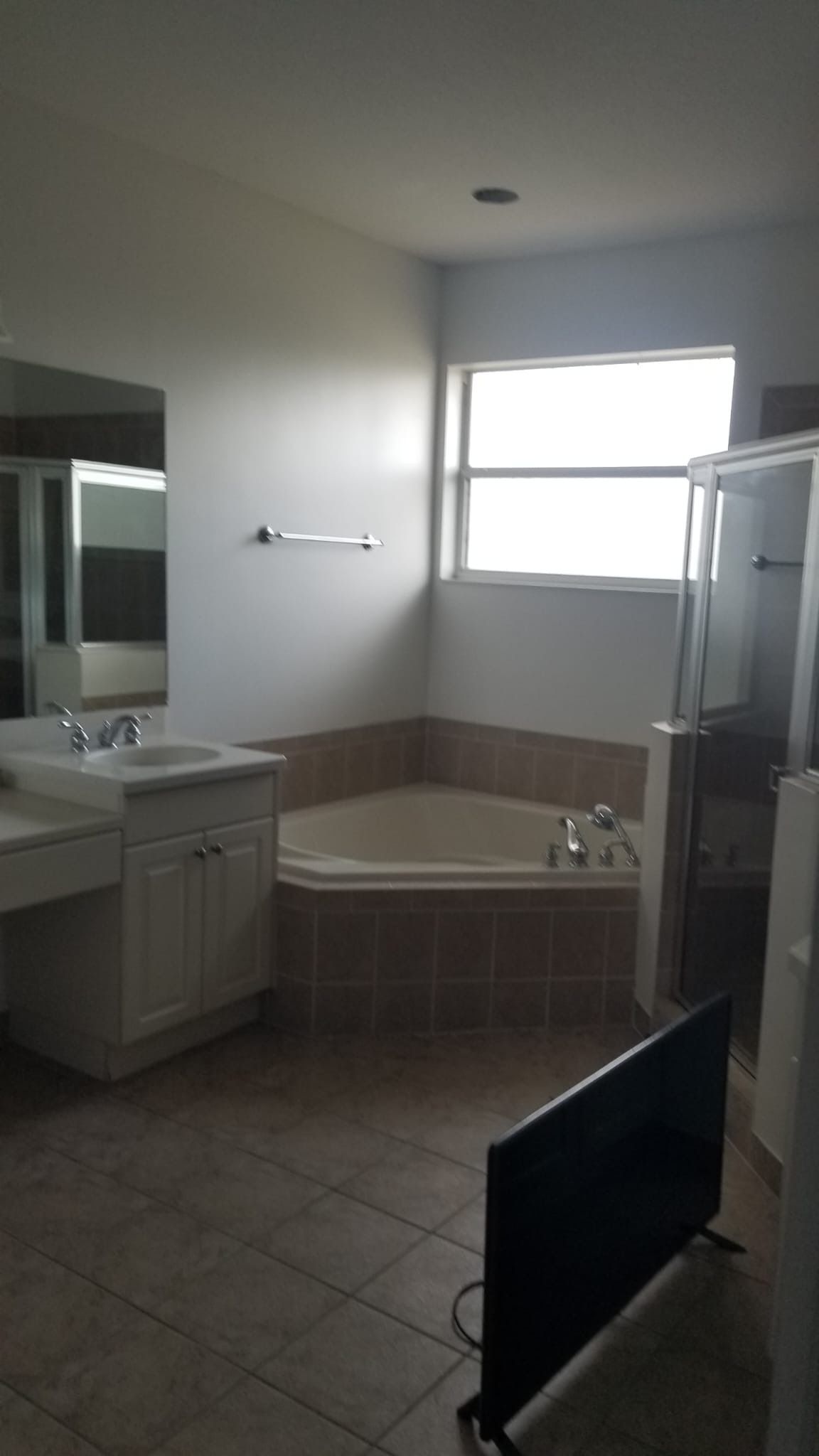 Bathroom with tub, shower, sink, and TV. Beige tile floor and light walls.