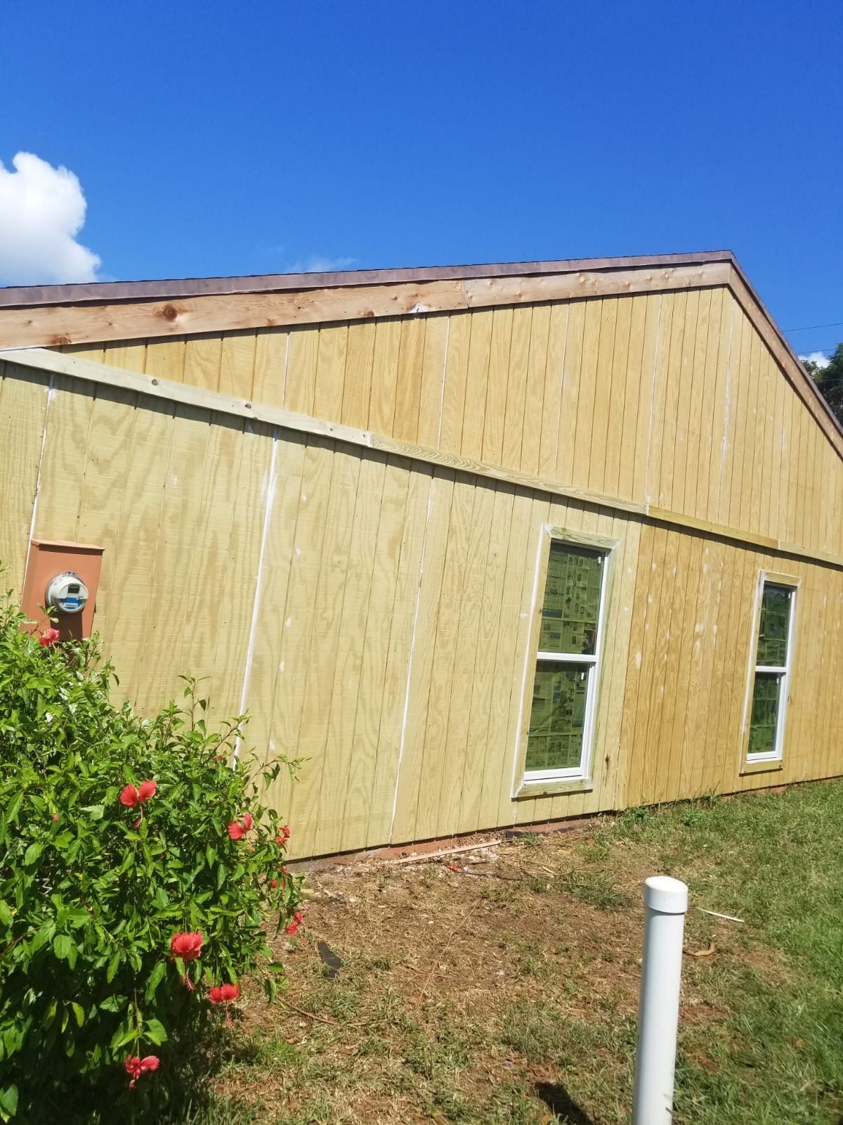 Exterior of a building with light wood siding and two windows, set against a bright blue sky.
