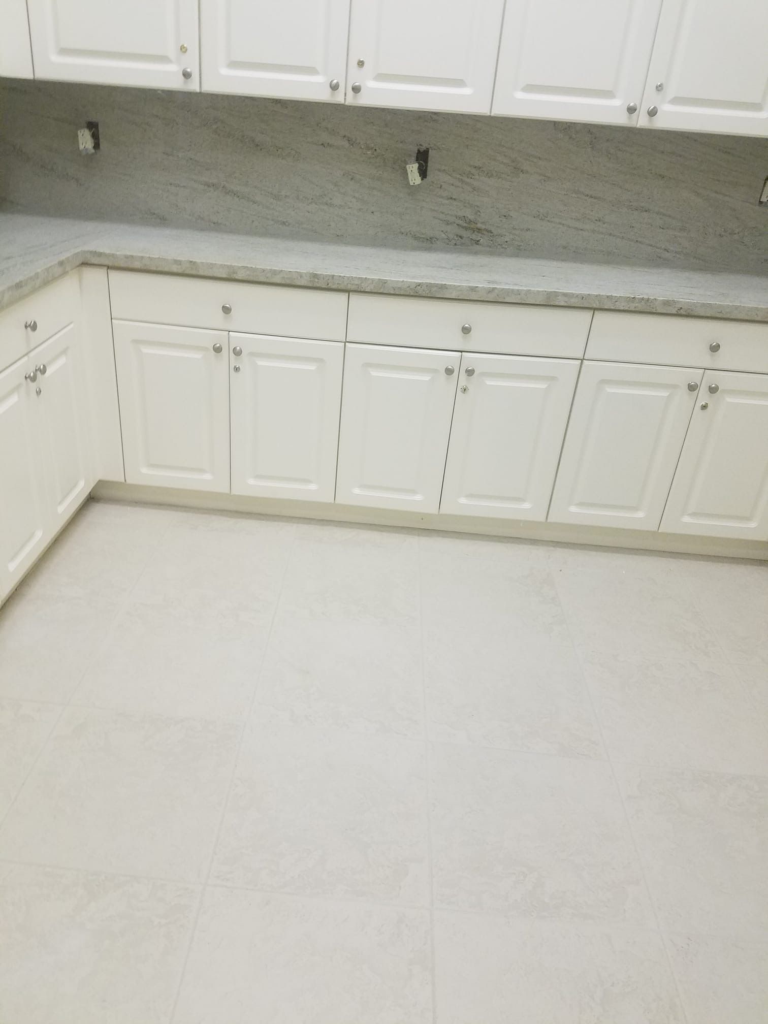 White kitchen cabinets with gray countertops and off-white tile floor.