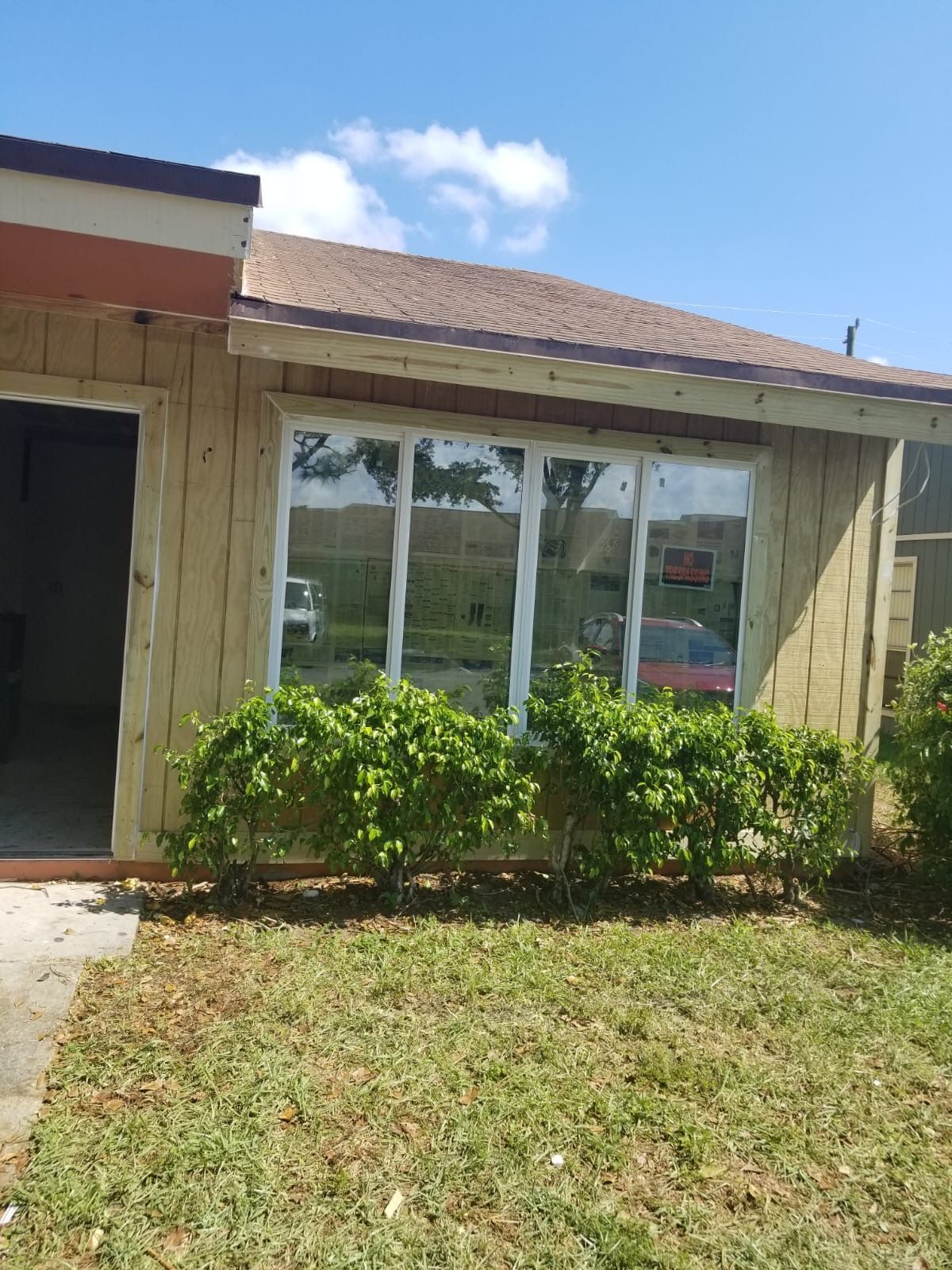 Exterior of a tan building with large windows, bushes in front, and a blue sky.