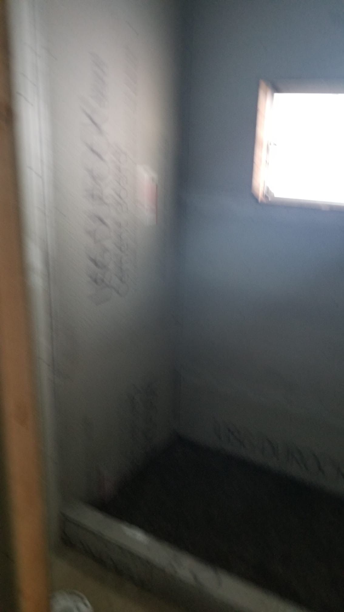 Empty shower stall, gray walls, small window, dark floor.