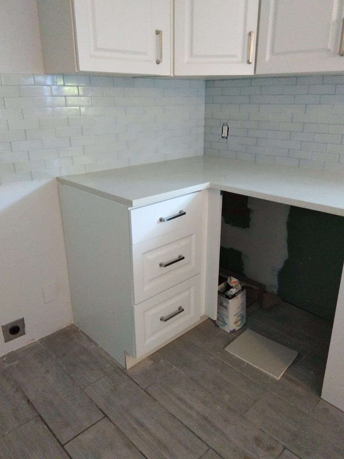 White kitchen cabinets with drawers and countertop; light blue tile backsplash; gray floor tiles.