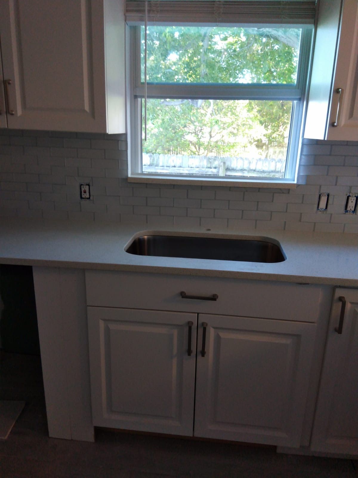 Kitchen with white cabinets, light countertop, and window above sink.