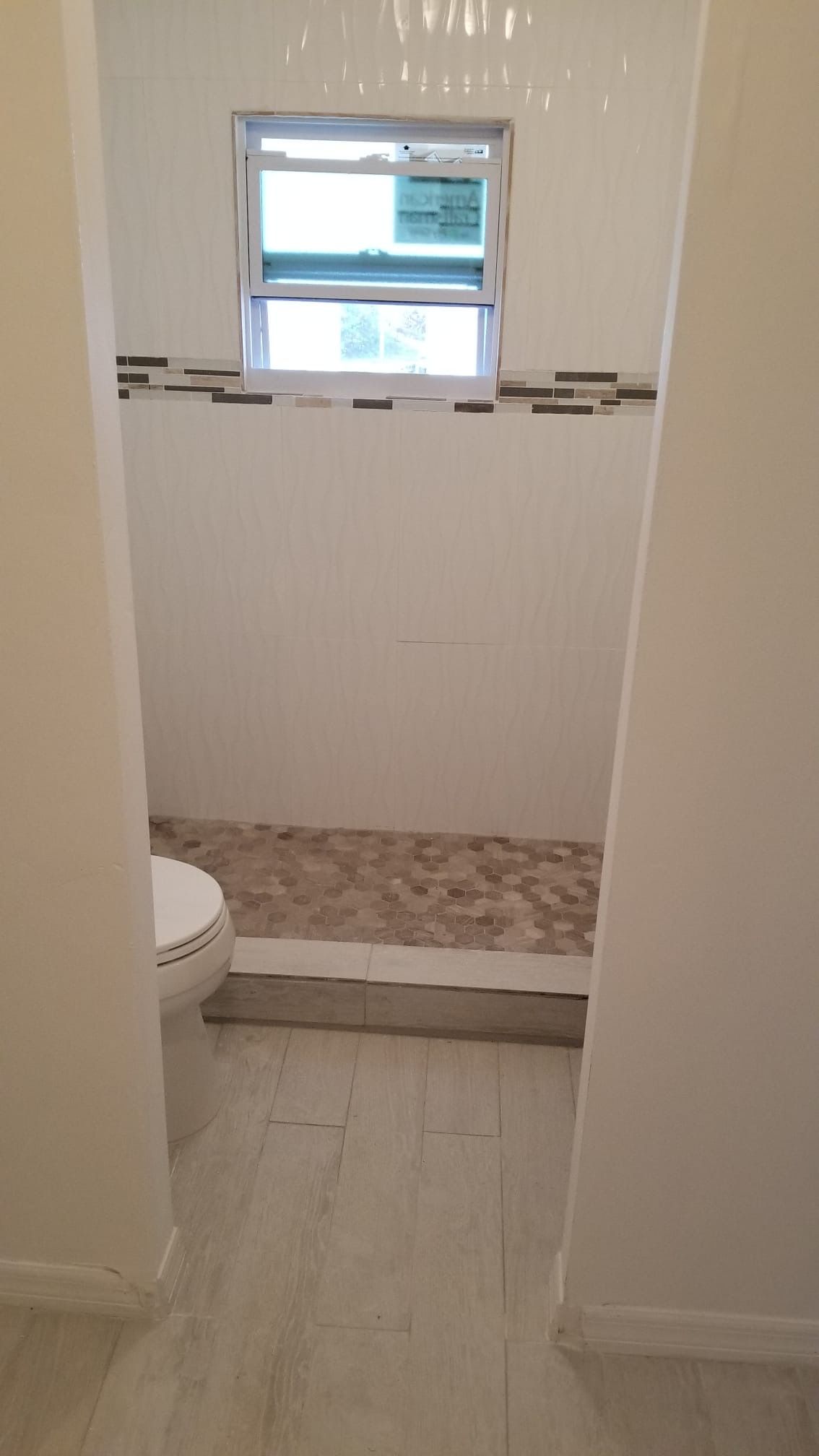 Bathroom with a shower, toilet, and window; white walls, neutral-toned floor and shower bed.
