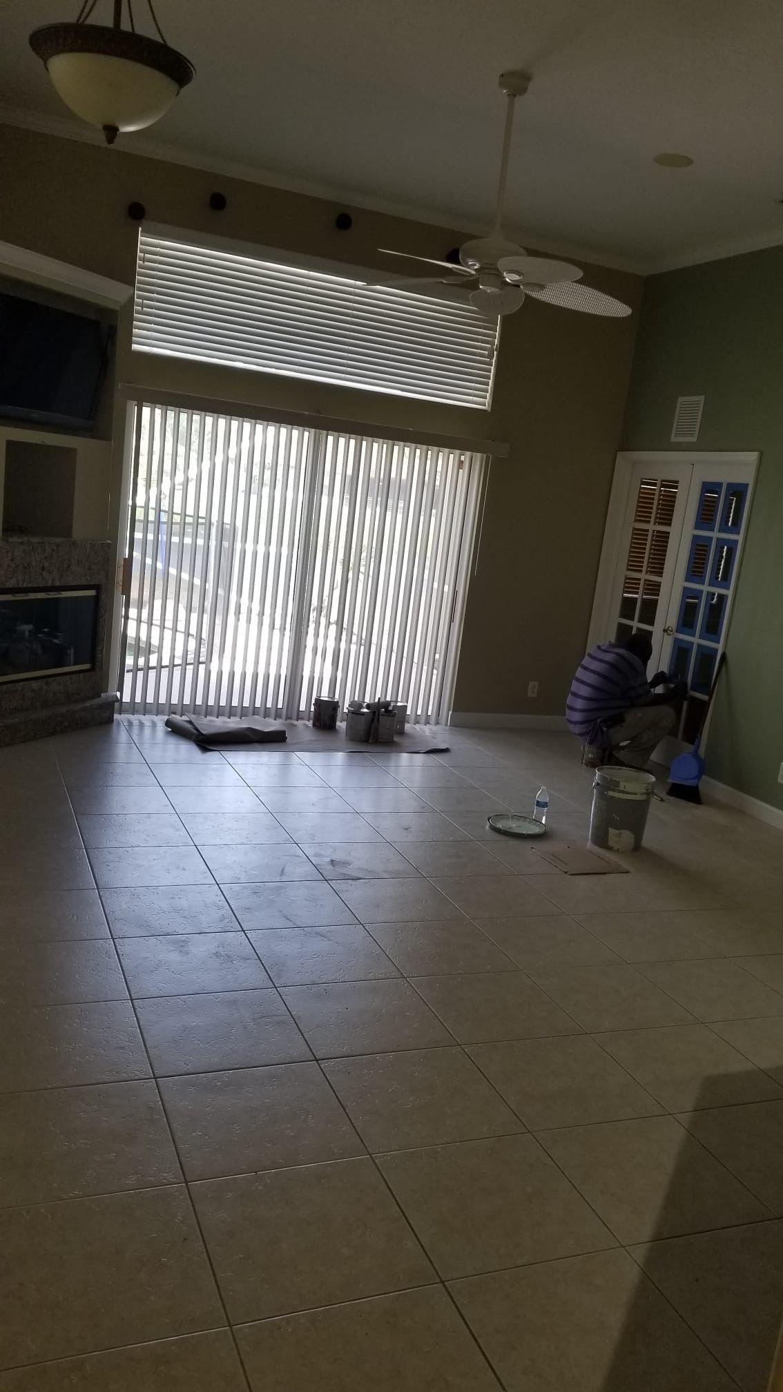 Living room with tiled floor, large window, fireplace, and person painting doors.