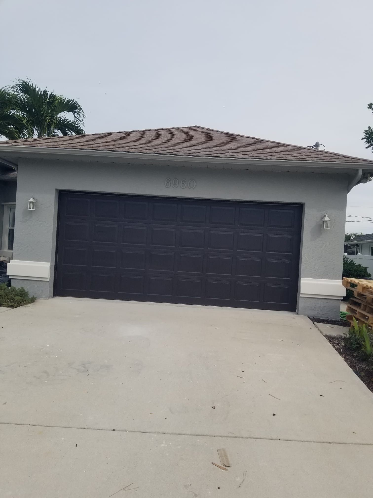 Gray house with brown garage door, concrete driveway, and brown roof under a cloudy sky.
