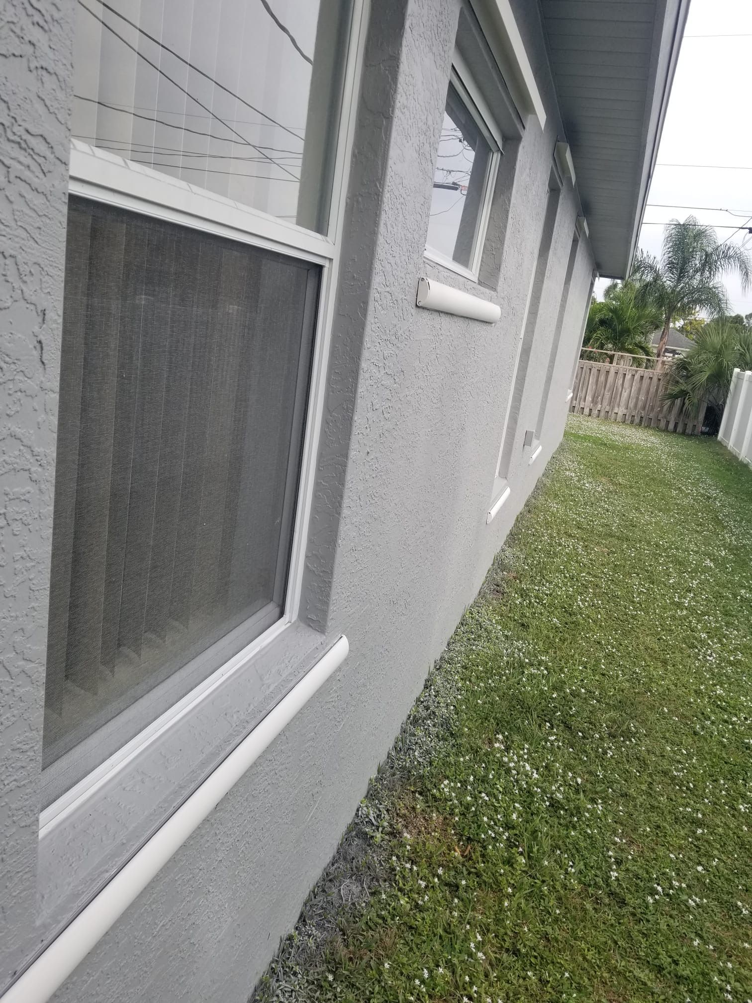 Exterior of a gray building with white-trimmed windows and a grassy yard with clover.