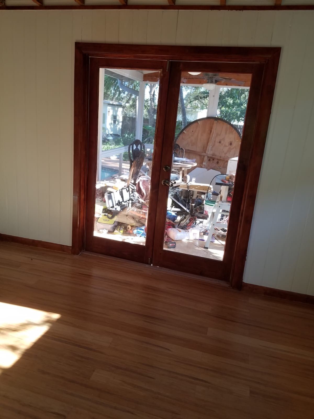 Wooden framed glass doors open to a cluttered porch with various items.
