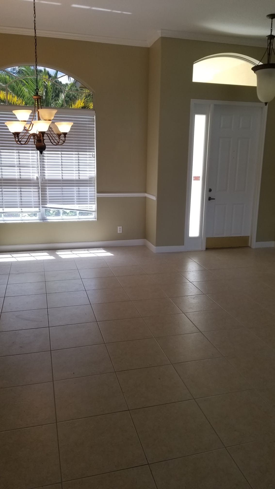 Empty interior room with beige walls, large arched window, and white front door.
