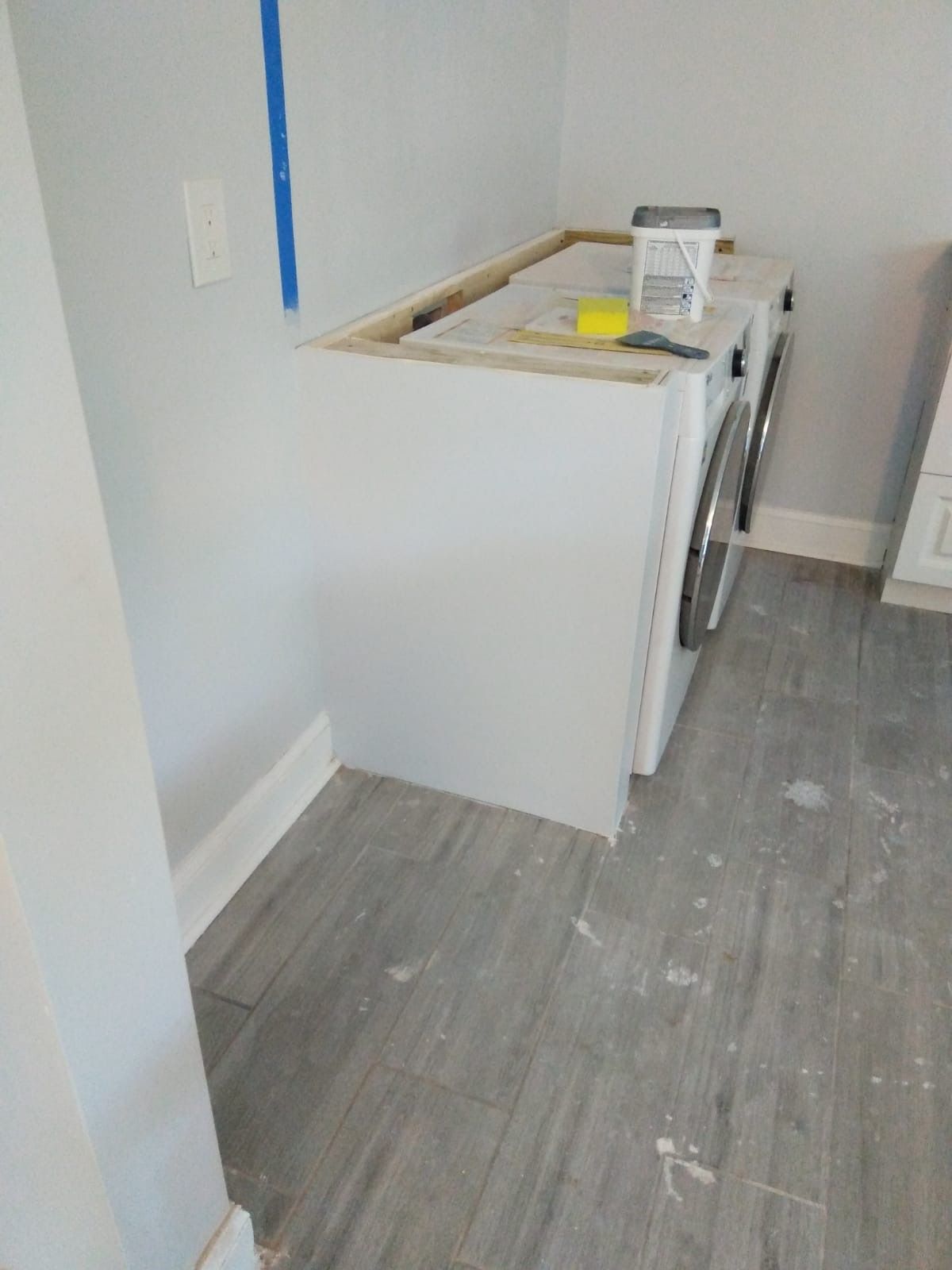 White laundry cabinets in a corner with a countertop, next to a washing machine and dryer, in a room with gray flooring.
