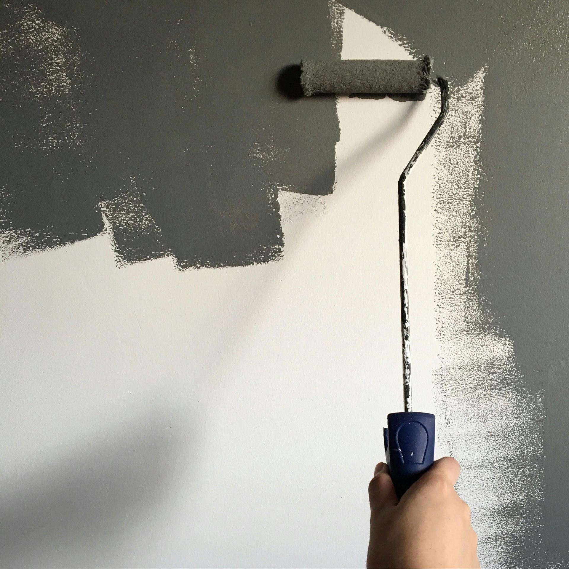 Person painting a white wall gray with a paint roller.