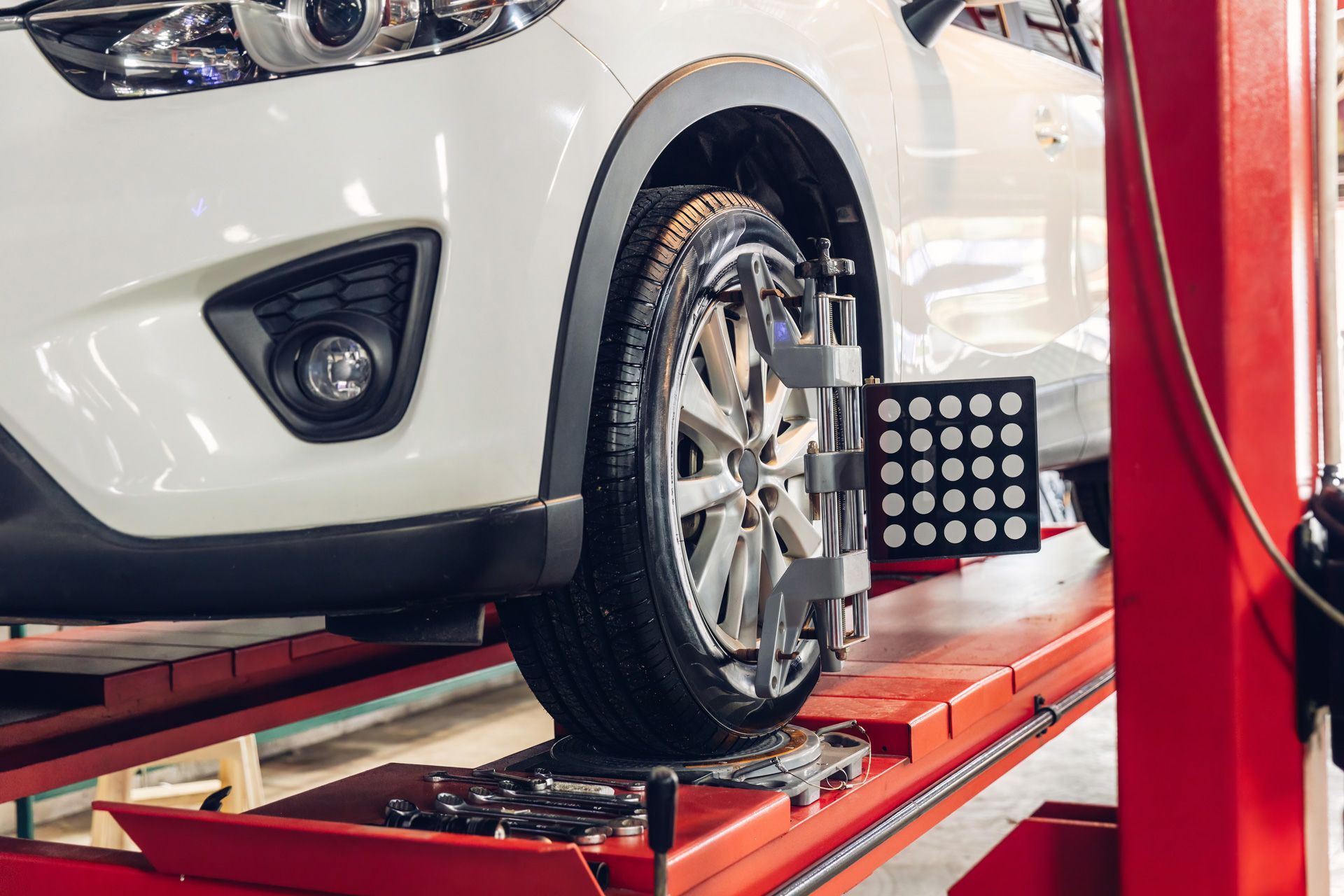 A white car is being adjusted on a lift in a garage.