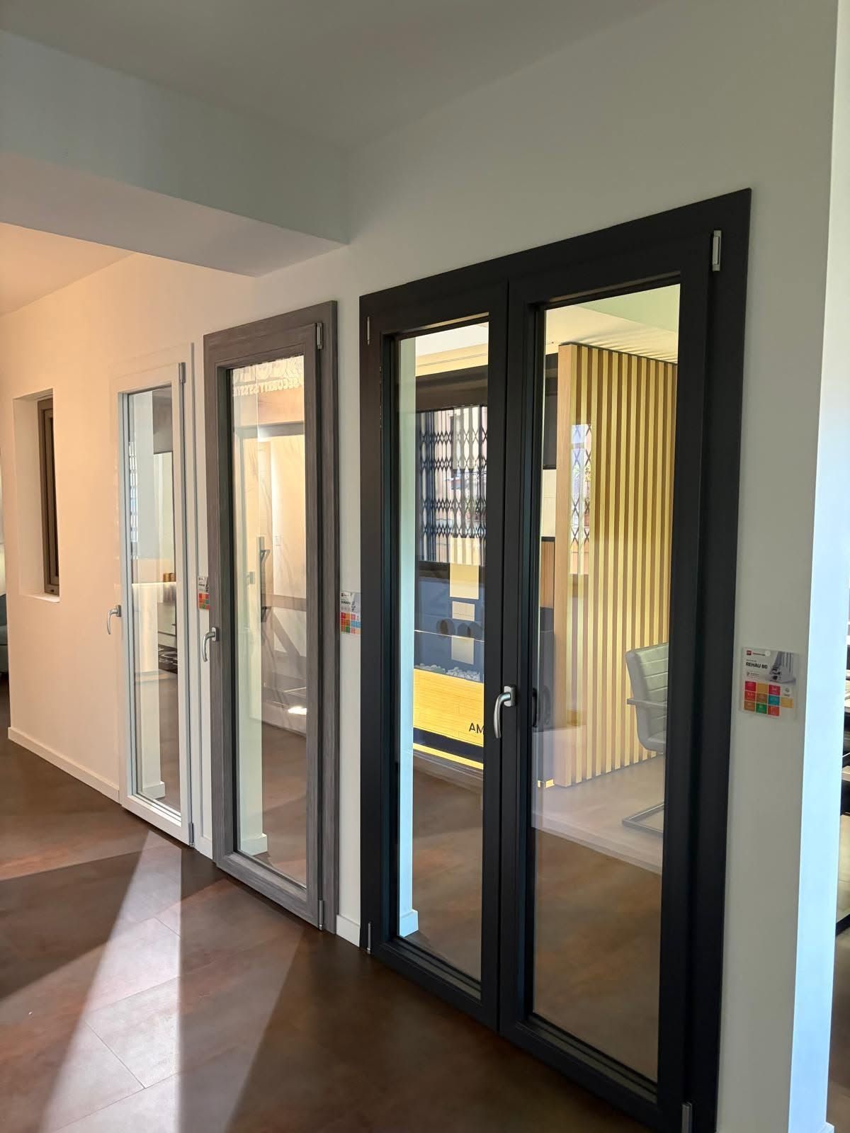 Corridoio interno con moderne porte in vetro e una stretta porta bianca accanto a un pavimento marrone.