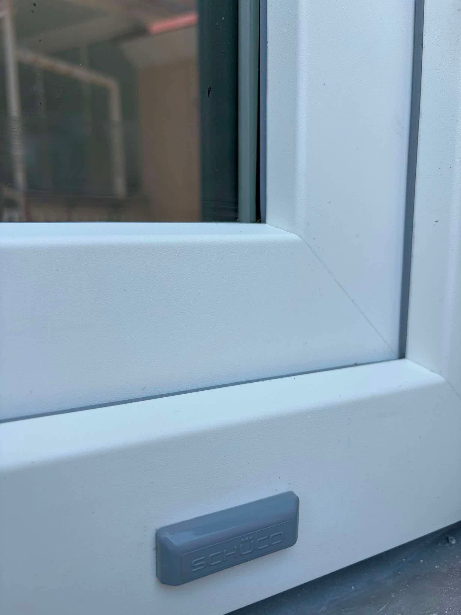 Angolo di una finestra o porta con cornice bianca e una piccola maniglia grigia in basso.