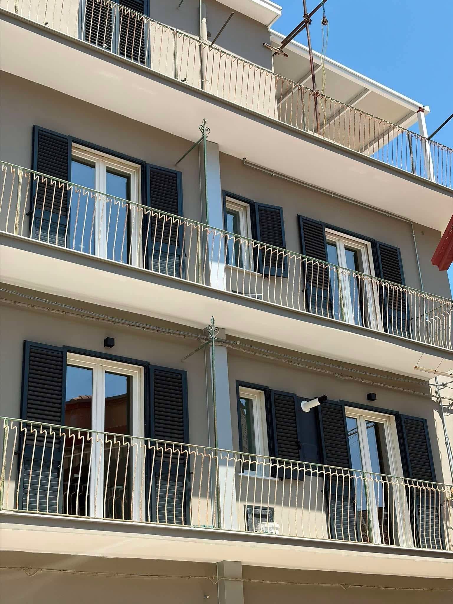 Balconi di un palazzo con ringhiere nere e persiane blu, illuminati dal sole splendente