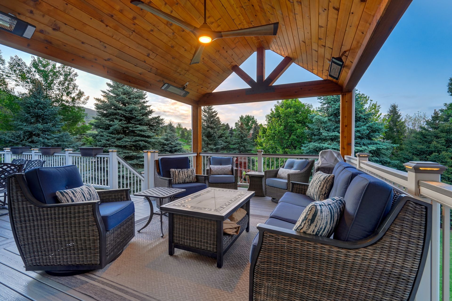 Covered patio with wicker seating around a coffee table, overlooking a backyard at sunset