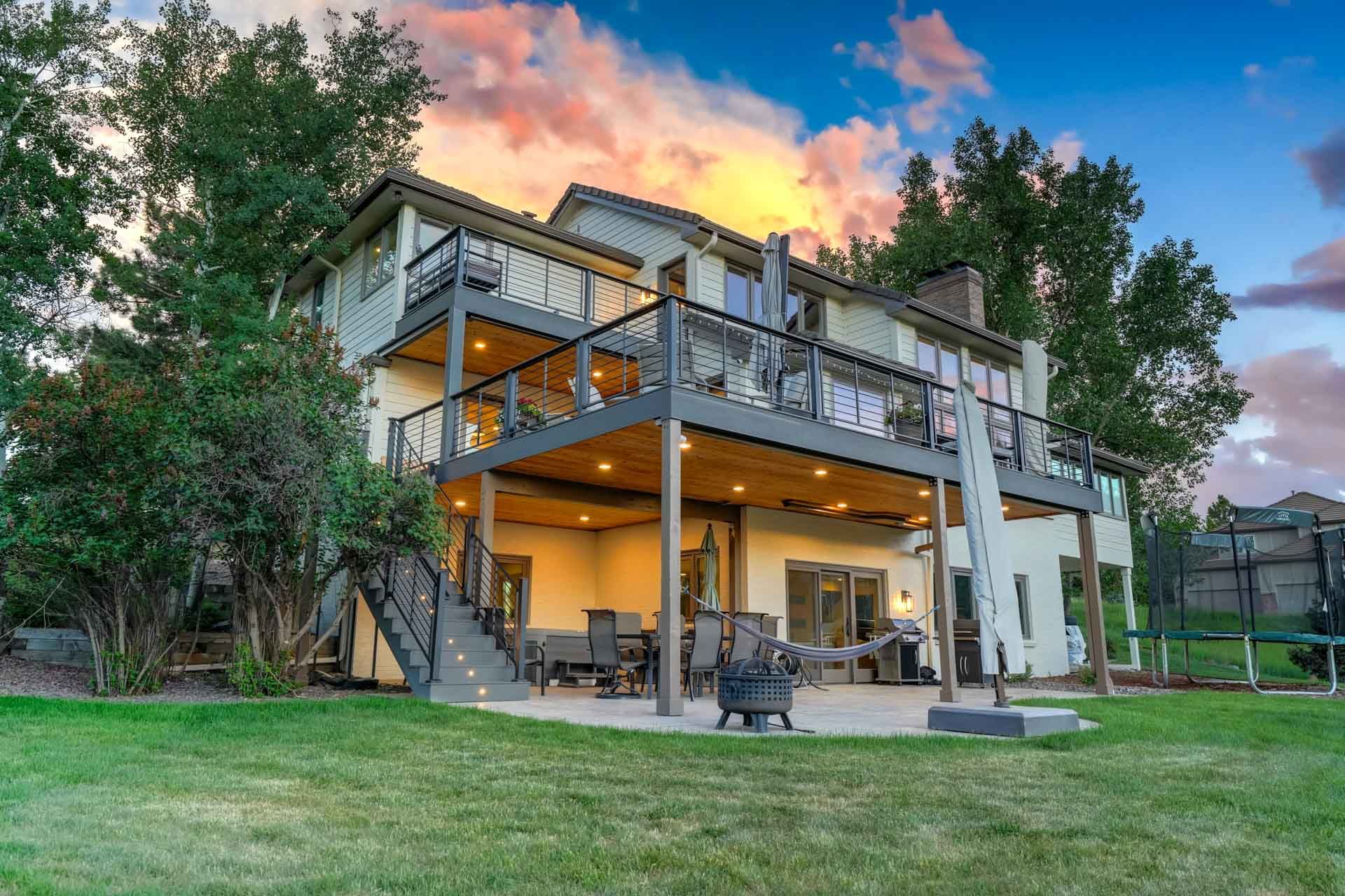 Large two-story house with a covered patio, deck, and lawn at sunset