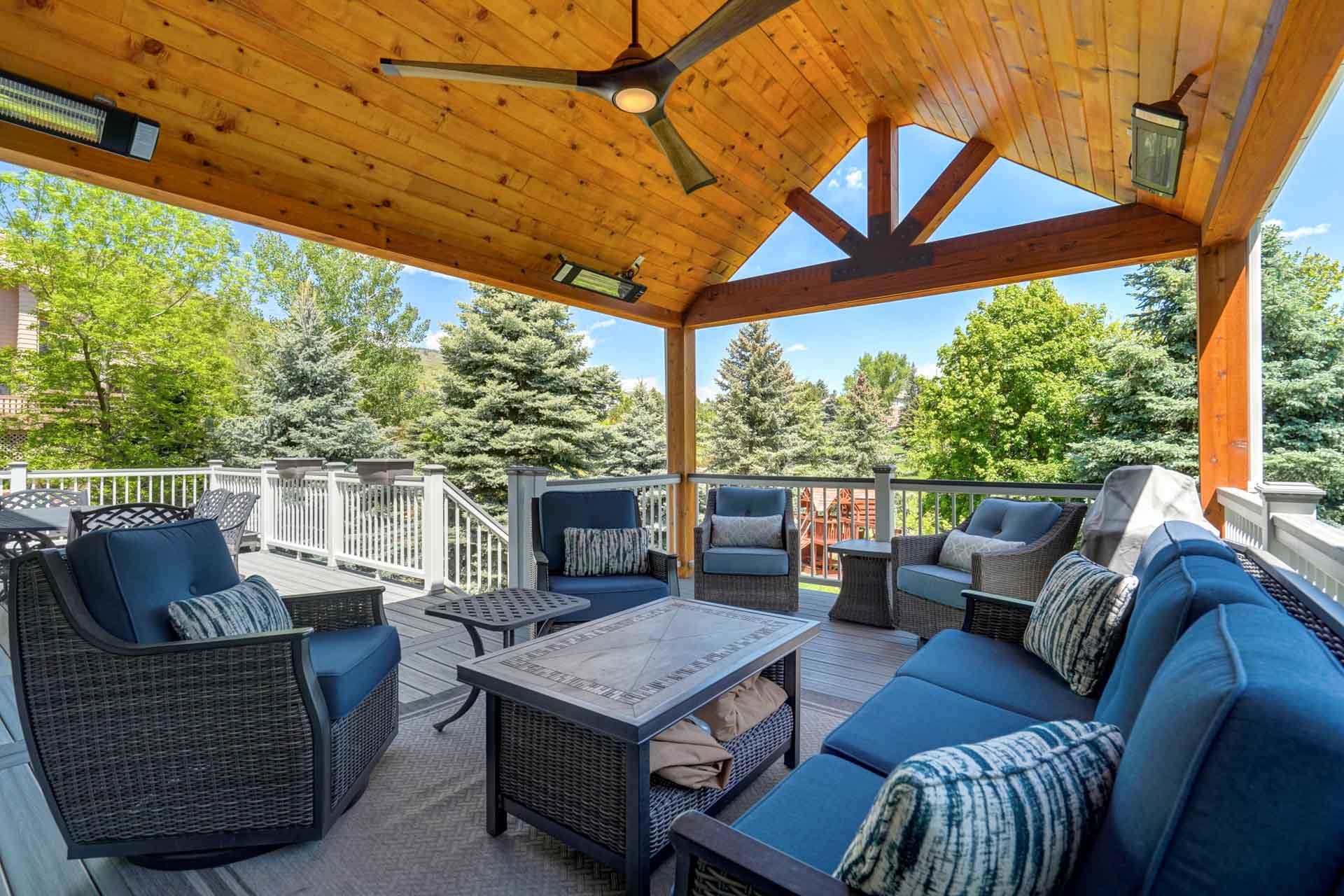 Covered backyard deck with wicker seating, coffee table, and a wood-paneled roof overlooking trees.