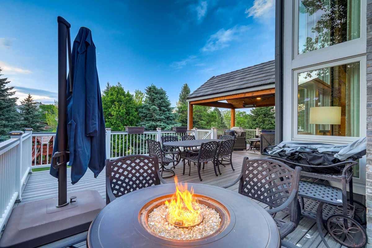 Patio with a lit fire pit, outdoor dining set, umbrella, and covered seating area overlooking a backyard