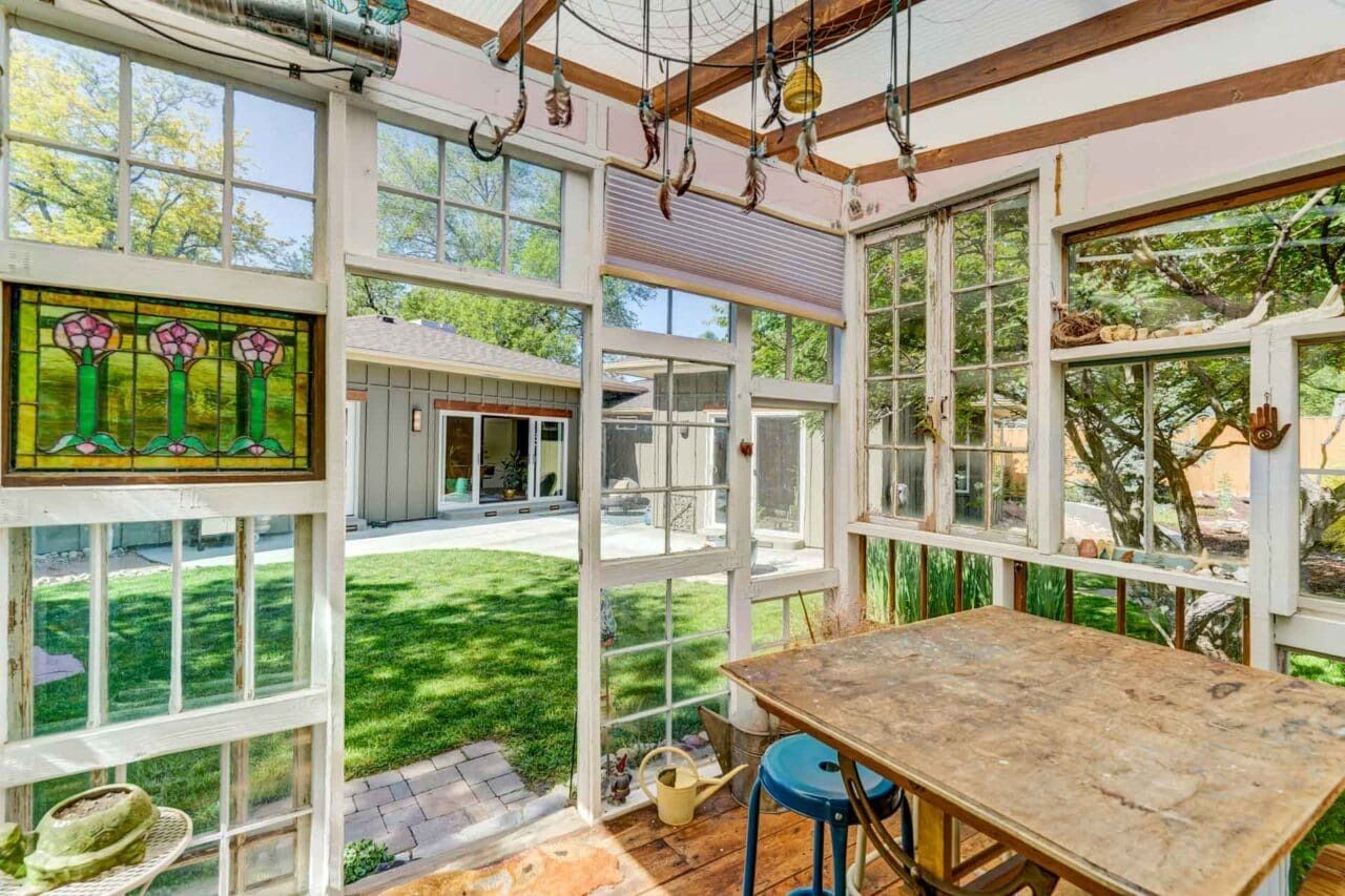 Sunlit glass sunroom with wood table, hanging lights, and a view of a green courtyard