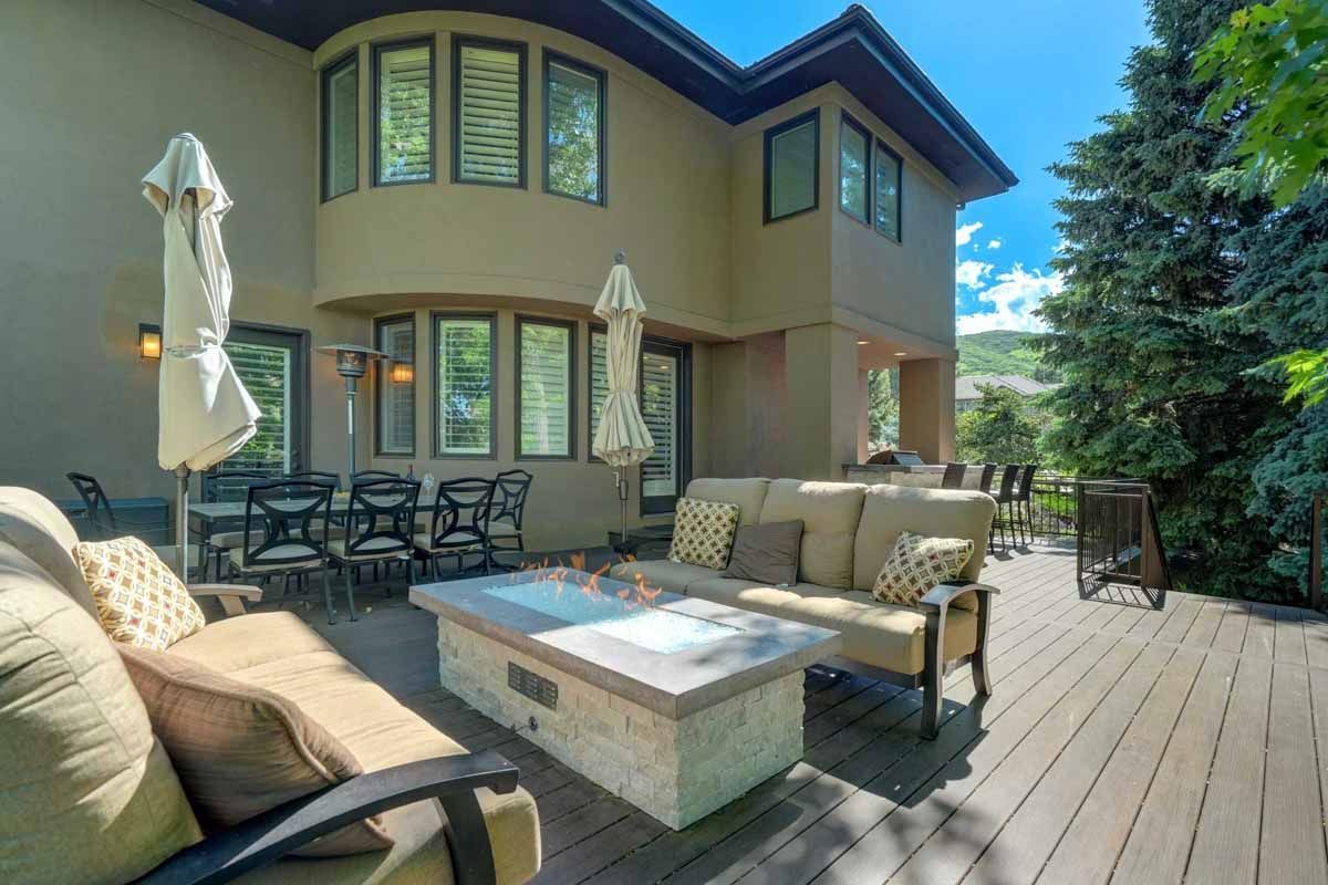 Modern patio with wicker seating, fire pit table, umbrellas, and a two-story house in the background