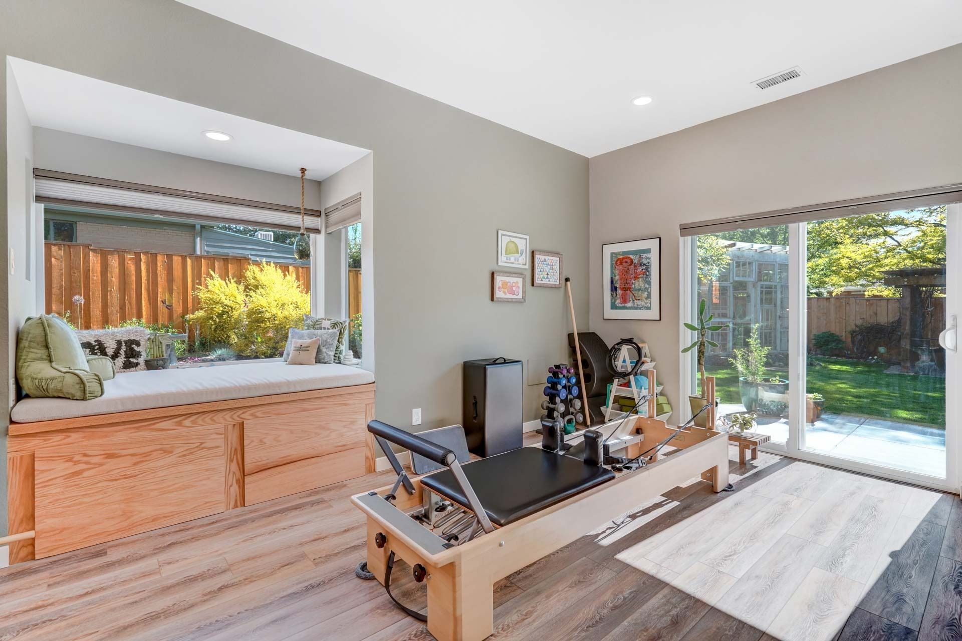 Bright living room with a window seat, desk, and sunlight from a glass door overlooking a garden