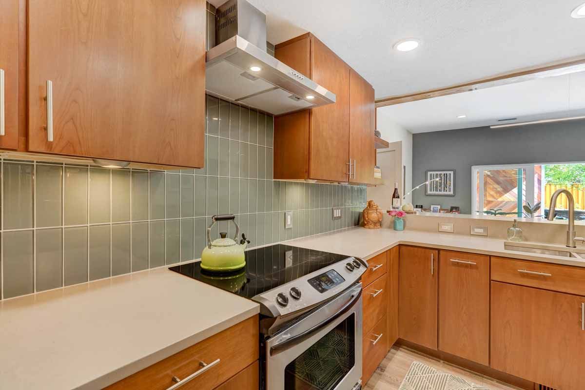 Bright kitchen with wood cabinets, stainless steel stove, tile backsplash, and a view into a dining area.