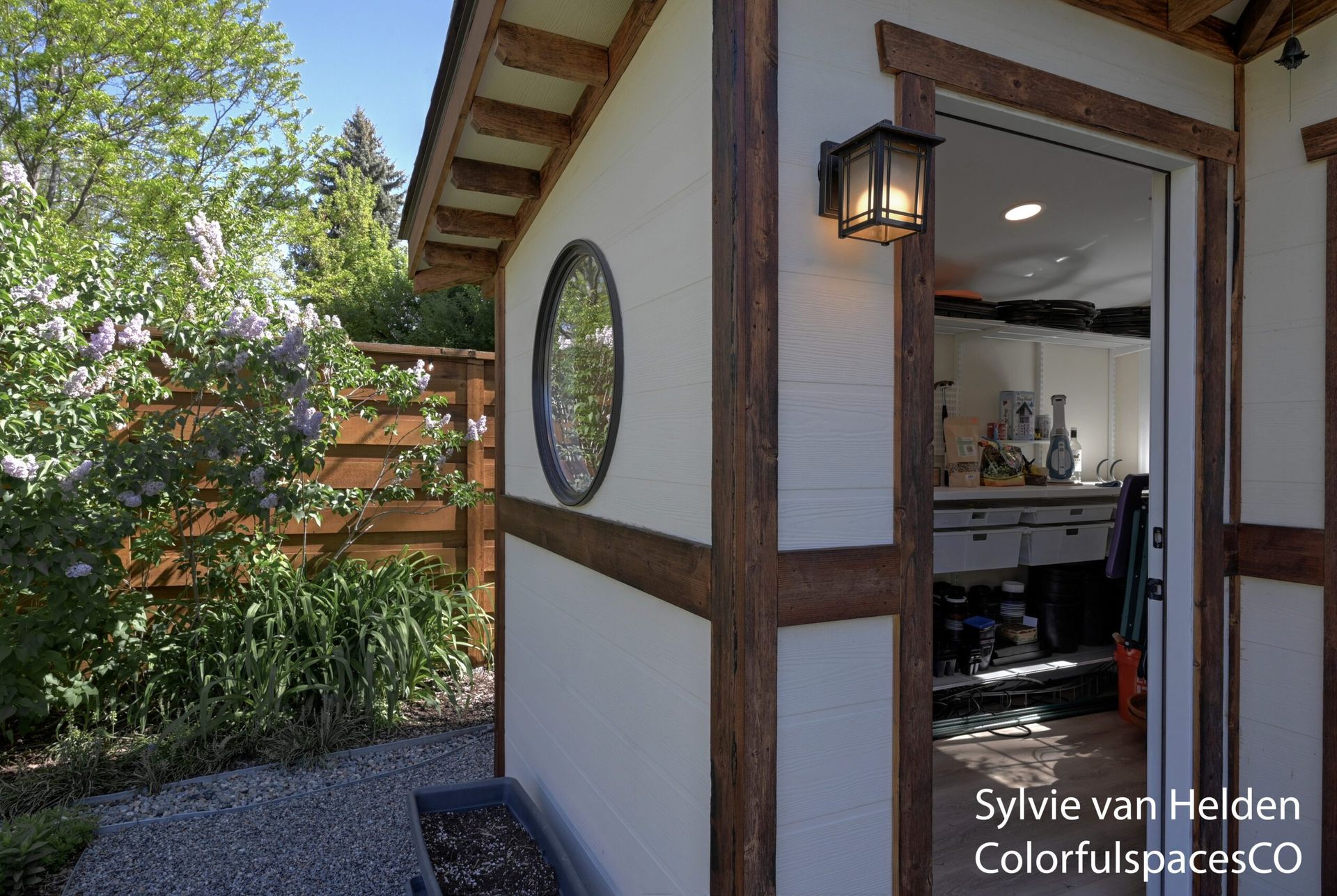 Open wooden door to a bright kitchen from a rustic garden patio with lantern and round window