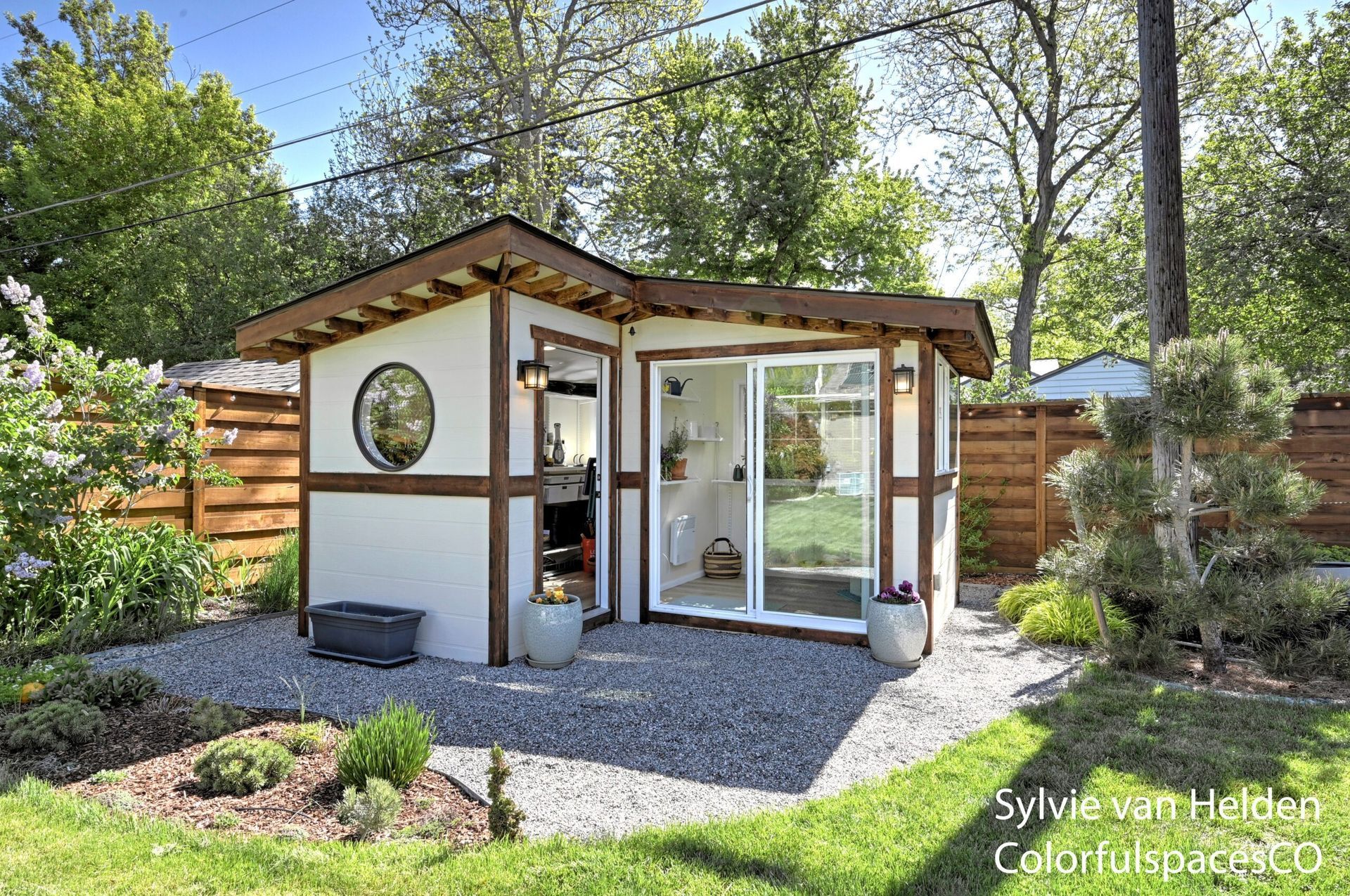 Modern backyard garden studio with glass sliding door, white walls, and gravel path surrounded by trees