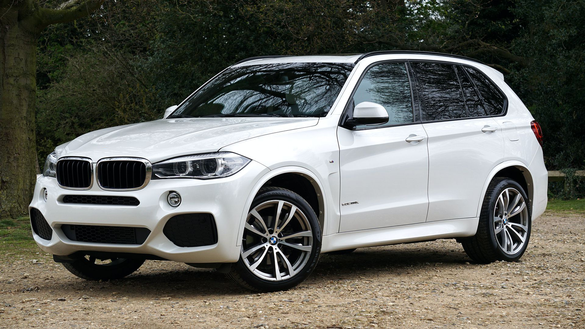 White BMW SUV parked on a gravel surface with trees in the background
