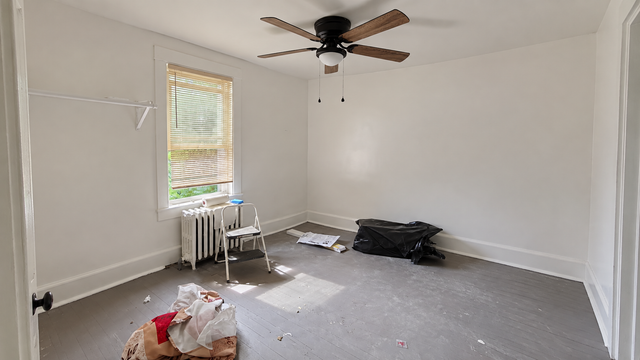 Empty white room with gray carpet, ceiling fan, window, and a few items on the floor