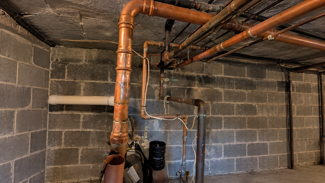 Basement with exposed copper pipes and HVAC ductwork along cinderblock walls