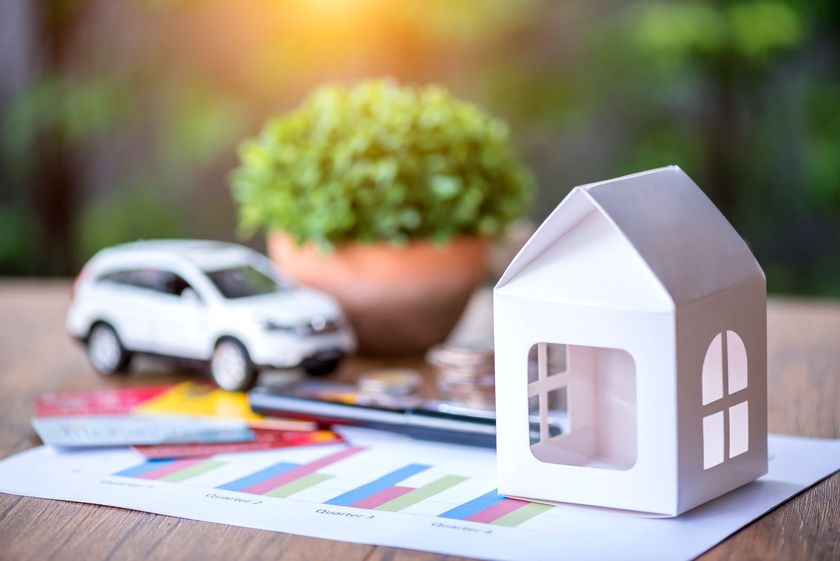 Paper house model with toy car and financial charts representing home and auto insurance.