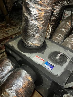 Insulated HVAC ductwork connected to a gray metal air handler in a cramped utility space