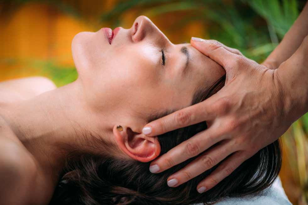 Person receiving a face massage with hands on the forehead and jaw, eyes closed, in a spa setting