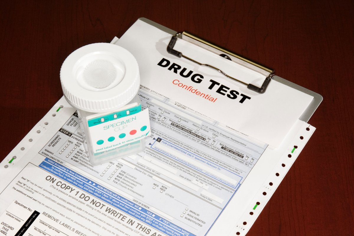 Drug test form with a specimen cup and rapid test kit on a table.
