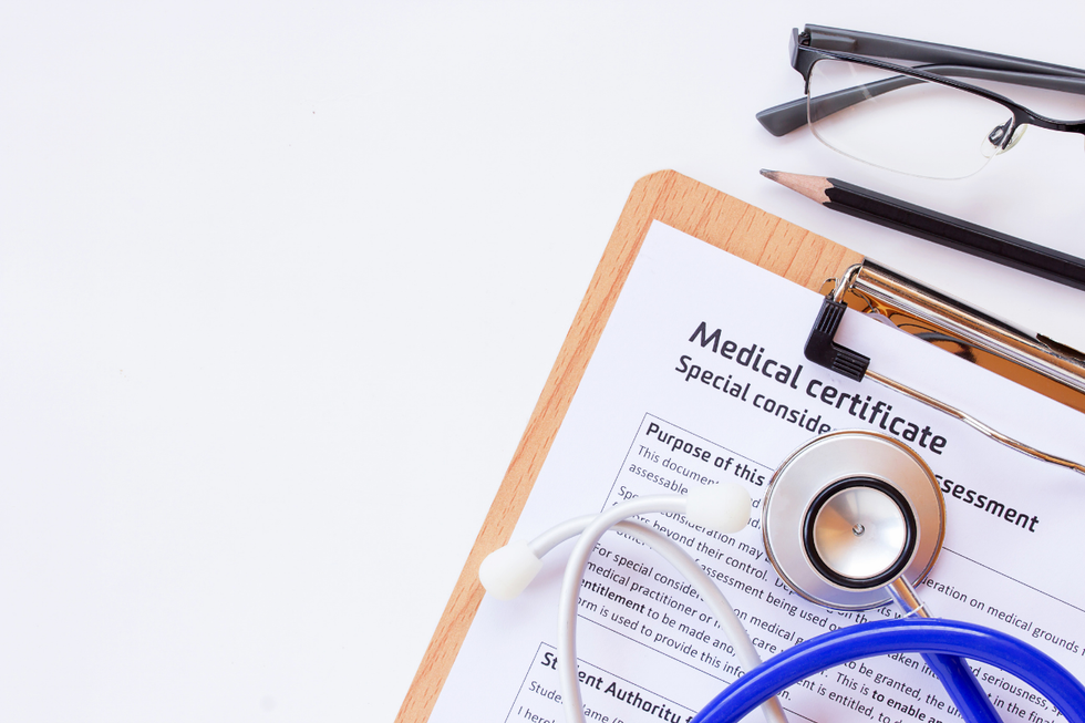 Medical certificate on a clipboard with a stethoscope and glasses on a white desk