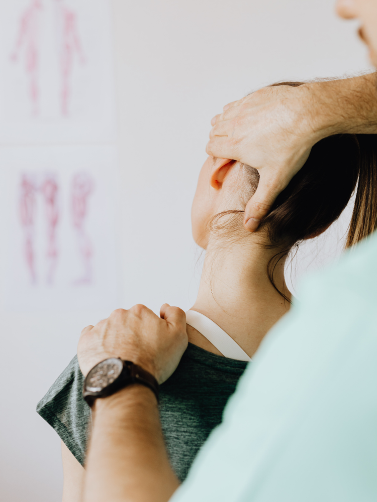 Hands massaging the neck of a person lying down, with a therapist in teal scrubs nearby