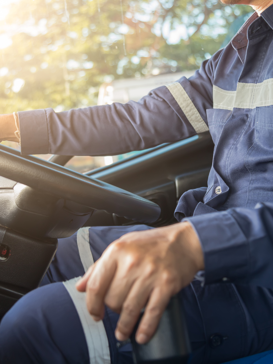 Driver seated at a wheel in a blue uniform, with sunlight streaming through the car window